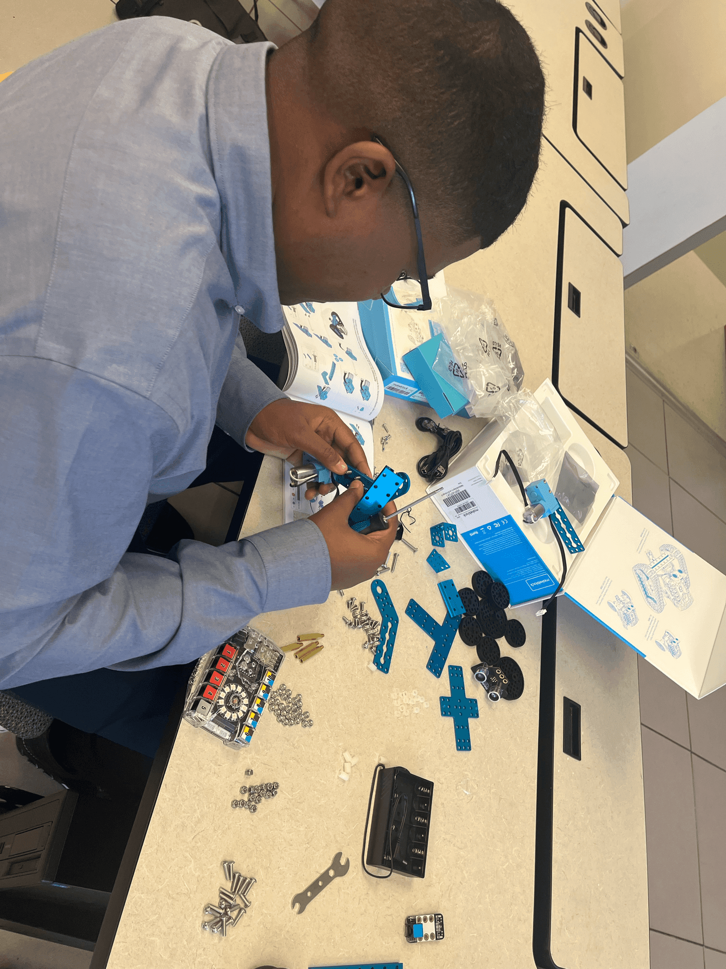 Person assembling a blue robot kit with various components and tools spread out on a table.